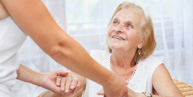 lächelnde ältere Frau im Stuhl wird fast die Pflegekraft an den Händen